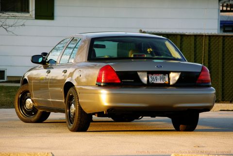 2005 Ford Crown Victoria - This gold Ford Crown Victoria is viewed from the rear, equipped with black steel wheels and a license plate.