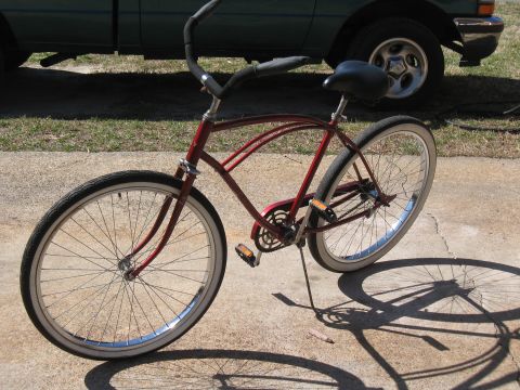 1994 Ford Bronco - A red cruiser bicycle casts a shadow on the concrete, with a portion of a green pickup truck visible behind it.