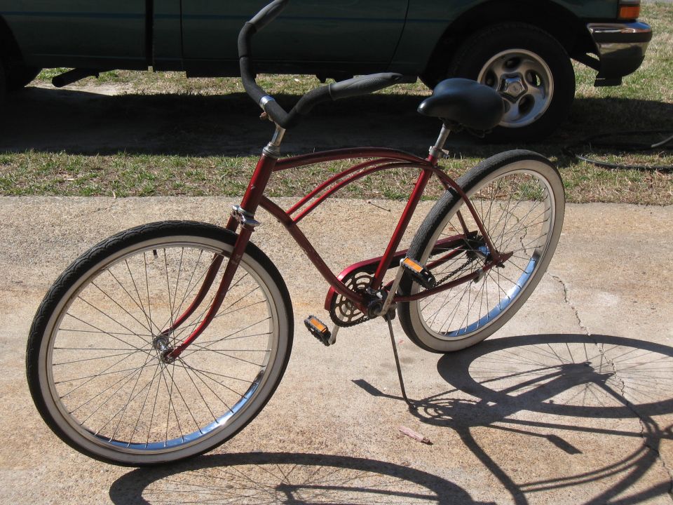 Red cruiser bicycle parked on concrete, with a green pickup truck in the background