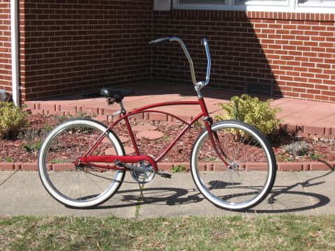 1994 Ford Bronco - A red cruiser bicycle with white-wall tires and tall handlebars is parked on a sidewalk in front of a brick house.