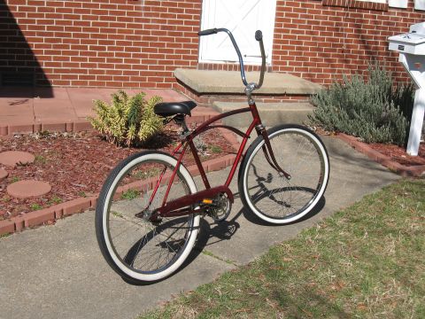 1994 Ford Bronco - A red cruiser bicycle with whitewall tires is parked on a sidewalk in front of a brick house.