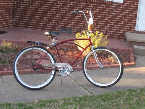1994 Ford Bronco - A red cruiser bicycle with whitewall tires is parked on a sidewalk in front of a brick house.