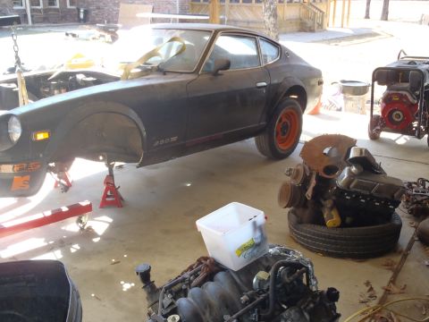 1978 Nissan 300ZX - A dark 1978 Nissan 300ZX coupe is shown on jack stands with its front end disassembled, surrounded by engine parts and a generator.