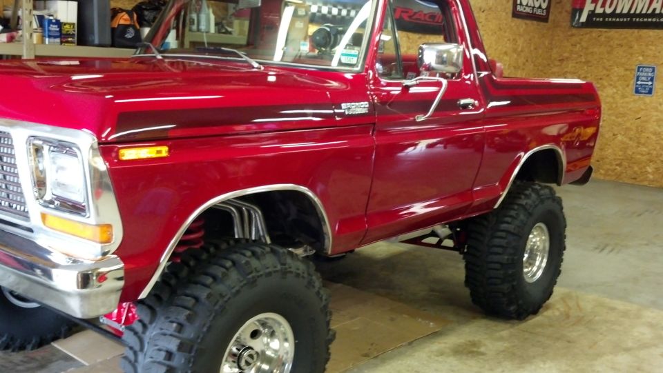 Lifted candy-red 1970s Ford Bronco on mud tires and chrome wheels in shop
