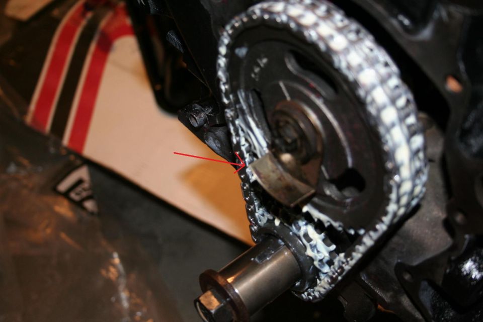 Close-up of engine timing chain and gears with a red arrow pointing to a spot