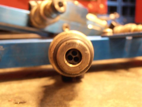 1990 Ford Bronco - A close-up view of a metal fuel injector nozzle with three openings, attached to a blue bracket.