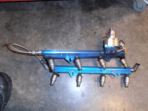 1990 Ford Bronco - pair of blue anodized aftermarket fuel rails fitted with injectors and a pressure regulator on a shop floor.