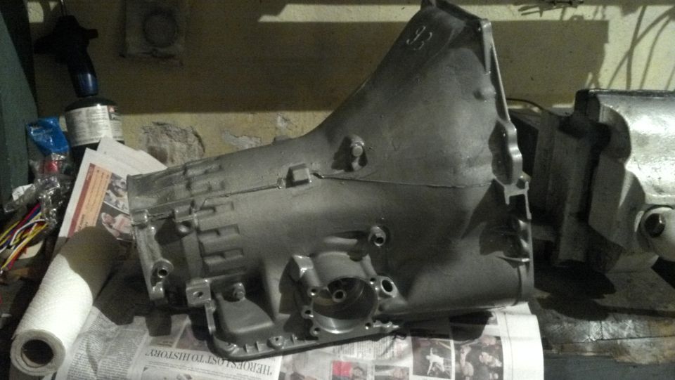 Gray metal transmission casing clamped in a vise, resting on newspapers