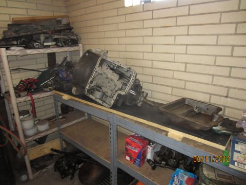 1979 Ford Bronco - Transmission assembly resting on a workbench, surrounded by various automotive parts and tools.