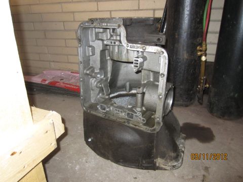 1979 Ford Bronco - A disassembled transmission case sits on the floor, with welding tanks and equipment in the background.