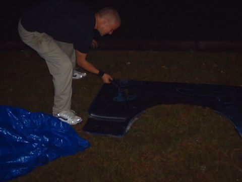 1990 Ford Bronco - Car fender with flame decals being handled by a person next to a blue tarp.