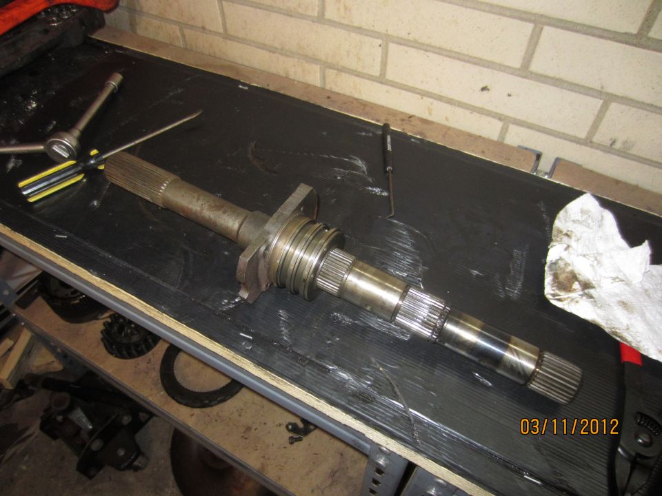 Transmission input shaft with splines on both ends, resting on a workbench with tools