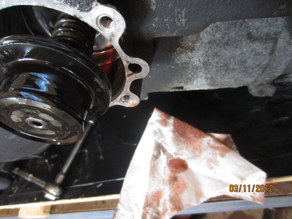 Close-up of a black transmission component with a spring, next to a paper towel stained with oil