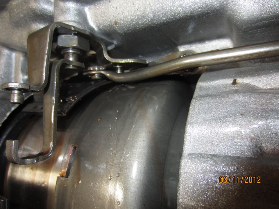 Close-up of a metal transmission linkage with bolts and a rod, showing some oil residue