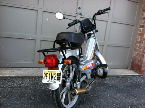 1999 Tomos Targa - Rear view of a silver moped parked in front of a garage door, displaying a New Jersey license plate.