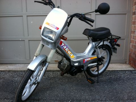 1999 Tomos Targa - A silver Tomos Targa moped is parked in front of a garage door, showing its 'Targa' and 'Tomos' branding.