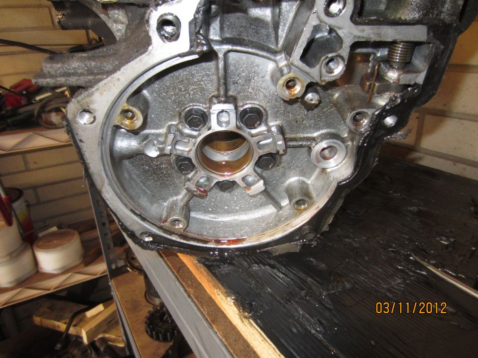 Close-up of an engine transmission housing with bolts and oil. Date stamp 03/11/2012