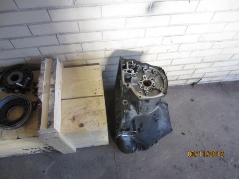 1979 Ford Bronco - A disassembled transmission housing and associated parts are shown next to a wooden crate on a concrete floor.