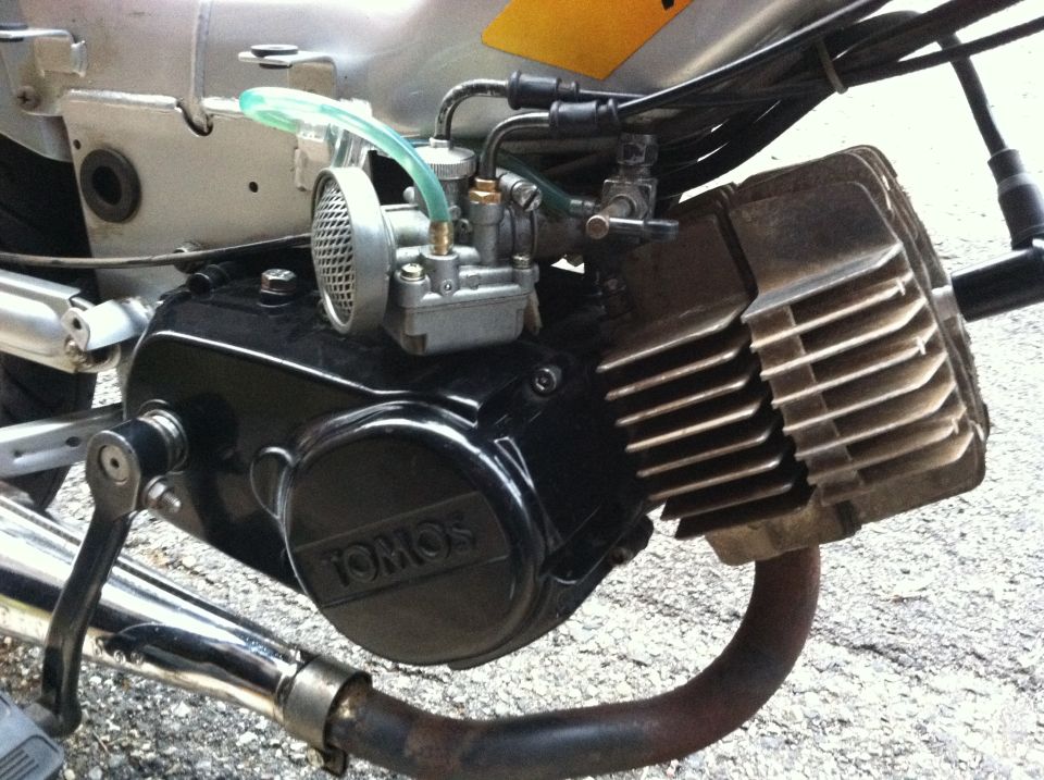 Tomos moped engine with carburetor and exhaust pipe. Black casing with 'TOMOS' logo