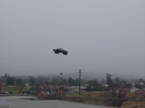 1996 Ford Bronco - An RC monster truck is captured mid-flight over a hazy, suburban landscape.