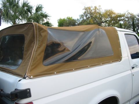 1992 Ford Bronco - The side profile of a white 1992 Ford Bronco is visible, fitted with a tan soft top.