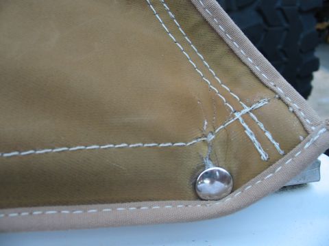 1992 Ford Bronco - Close-up of a tan soft top corner with visible stitching and a snap, with a tire in the background.