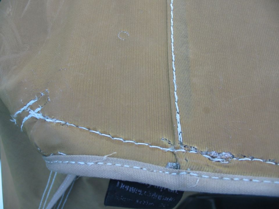 tan fabric with white stitching, some fraying and a small hole. A black tag is visible