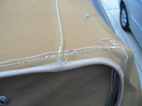 1992 Ford Bronco - Close-up of a tan soft top showing wear and tear on the stitching, with a car wheel visible in the background.