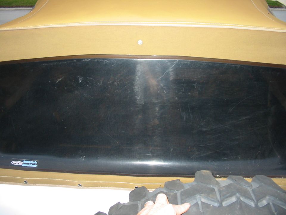 Close-up of a tan soft top on a vehicle, with a black plastic trim piece and a large tire tread visible
