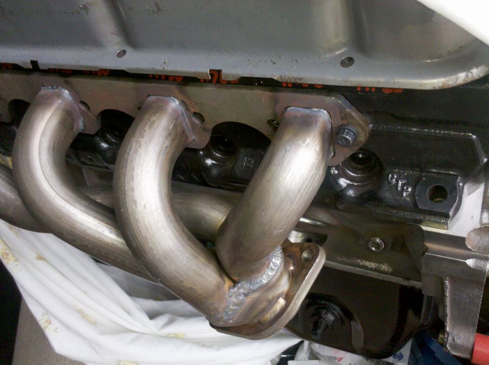 Close-up of a newly welded exhaust manifold attached to a black engine block