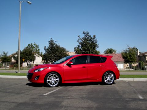 1989 Mazda MX-6 - A red hatchback is parked in a lot on a sunny day with houses and trees in the background.