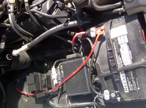 2000 Ford Crown Victoria - Close-up of a car battery and engine bay wiring, showing electrical connections and hoses.