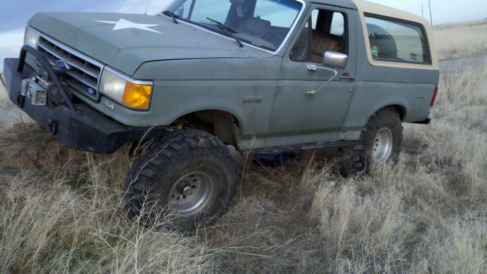 Modified Ford Bronco with aftermarket bumper and winch, parked in dry grass