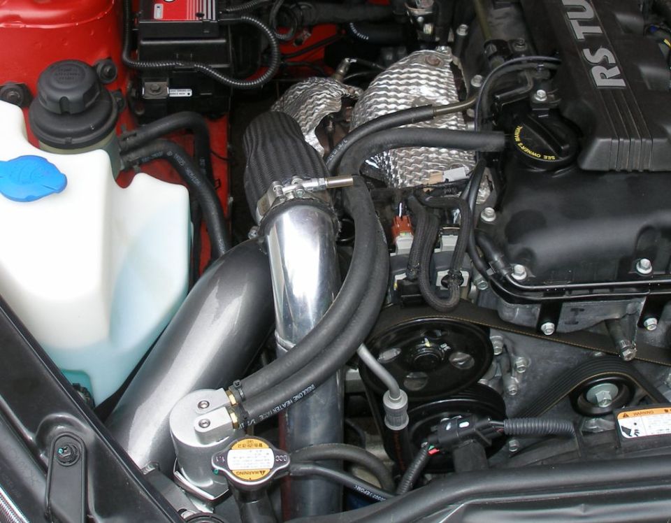 Engine bay with aftermarket catch can, air intake, and heat shielding. A blue cap is visible on a white fluid reservoir