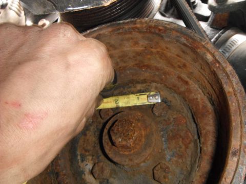 1988 Ford Bronco - A tape measure is used to check the diameter of a heavily rusted pulley, likely in an engine bay.