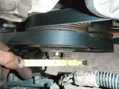 1988 Ford Bronco - A hand holds a measuring tape near engine pulleys and a belt, suggesting a part measurement.