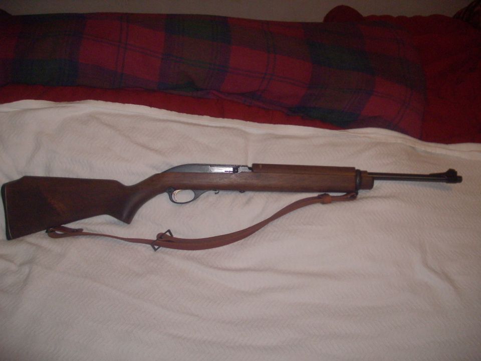 Wood-stocked rifle with leather sling on white bedding