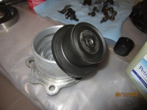 1979 Ford Bronco - A pulley and its housing are shown disassembled on a workbench, with various bolts and a bottle of petroleum jelly in the background.