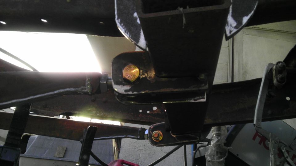 Close-up of rusty vehicle frame with bolted suspension parts and bright light source