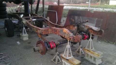 1987 Ford Ranger - A heavily rusted truck chassis is elevated on jack stands, revealing its front suspension system.