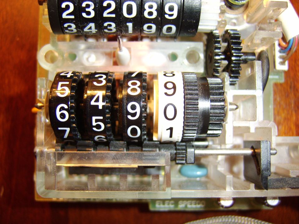 Disassembled mechanical odometer with number wheels and gears on a wood surface