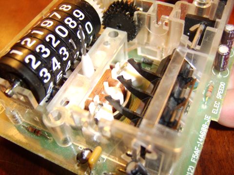 1996 Mercury Grand Marquis - Close-up of a disassembled speedometer odometer showing the mechanical odometer rollers and electronic circuitry.