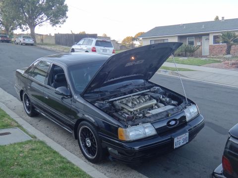 1993 Ford Taurus - The hood of this black sedan is open, revealing its engine and a 'SHO' emblem on the underside of the hood.