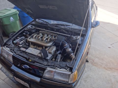 1993 Ford Taurus - The engine bay of a black 1991 Ford Taurus SHO is visible with the hood open.