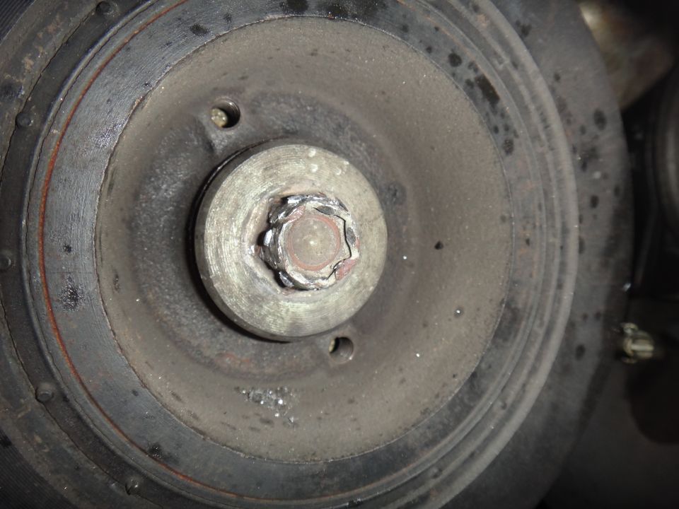 close-up of a crankshaft pulley bolt on a dirty engine part