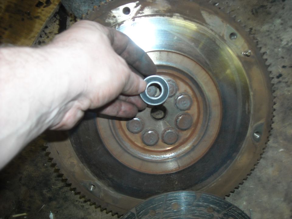 Hand holding pilot bearing over flywheel with clutch disc visible below