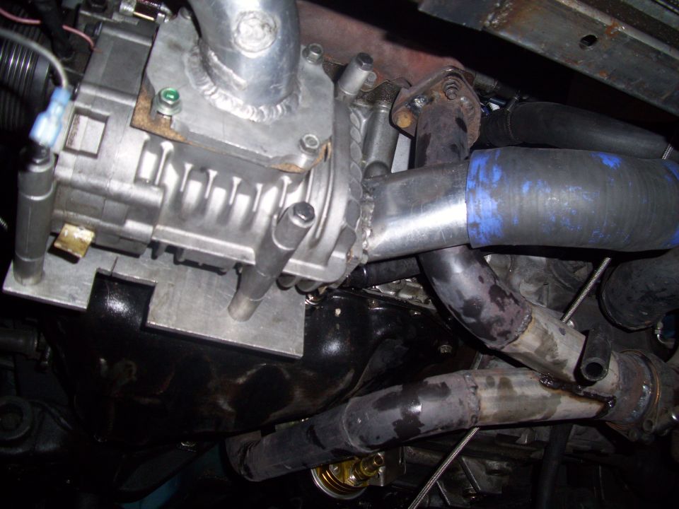 Close-up of a supercharger bolted to an engine, with various pipes and hoses connected