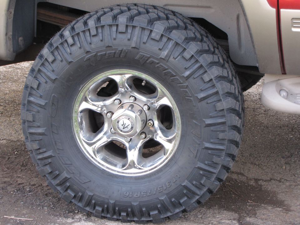 Polished alloy wheel with LT315/75R16 Trail Grappler mud tire on tan truck
