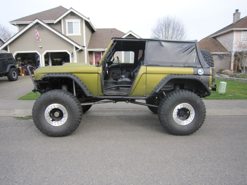 Olive green Ford Bronco with large off-road tires and a soft top, parked in a driveway