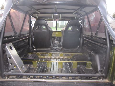 1974 Ford Bronco - The interior of a heavily modified SUV, viewed from the rear, showing racing seats and a roll cage.